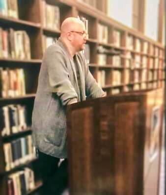 Jason Kapcala standing at a podium in a library, reading